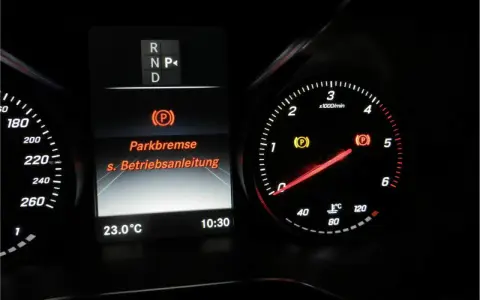 Mercedes-Armaturenbrett: gelbe Warnleuchte für die Feststellbremse leuchtet. Die Anzeige "Parkbremse" und "s. Betriebsanleitung" ist sichtbar.