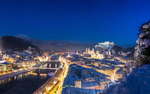 Magiczne salzburg zimą. Oświetlone miasto, rzeka Salzach i górująca twierdza Hohensalzburg w śnieżnej scenerii nocą.