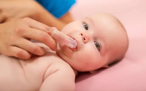Delikatne czyszczenie ząbków niemowlaka specjalną nakładką na palec. Pokazuje, jak myć zęby niemowlakowi.
