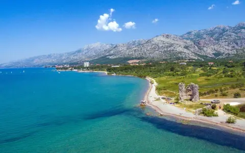 Piękne wybrzeże z górami w tle, idealne na camping Paklenica. Woda kusi turkusowym kolorem, a na plaży widać ruiny starej twierdzy.