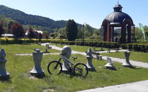 Rower czeka na ścieżce w Piwnicznej-Zdroju, wśród kamiennych figur i zieleni.