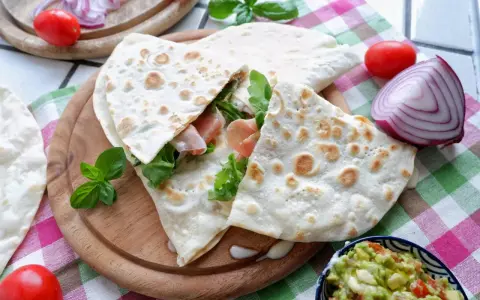 Piadina, piatto tipico di Rimini, farcita con prosciutto e rucola, servita con guacamole e verdure fresche.