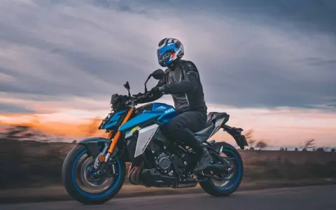 Motocyklista w kasku jedzie na niebieskim Suzuki GSX-S1000 podczas zachodu słońca.
