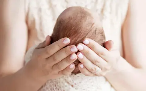 Mani delicate che accarezzano la testa di un neonato, proteggendo la sua fontanella.
