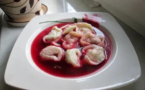 Pyszne uszka z mięsem pływają w czerwonym barszczu na białym talerzu.