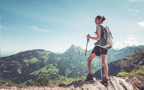 Dziewczyna z plecakiem i kijkami do trekkingu podziwia górski krajobraz. To jest właśnie hiking – przygoda na łonie natury.