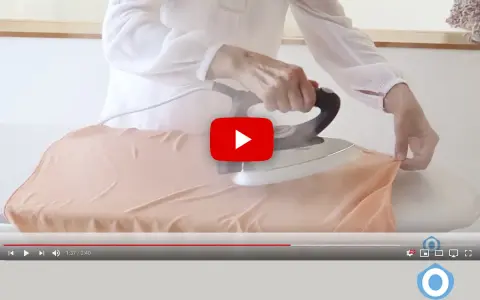 Manos planchando tela de viscosa con vapor en una tabla de planchar.
