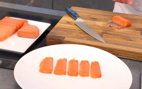 Filetes de salmón marinado listos para servir. Un cuchillo y una tabla de cortar de madera sugieren preparación.