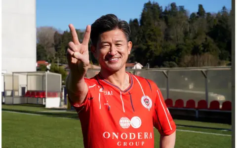 Uśmiechnięty Kazuyoshi Miura, najstarszy piłkarz na świecie, pokazuje znak pokoju na boisku.