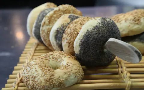 Une rangée de bagels faits maison, certains recouverts de graines de sésame, d'autres de pavot, sur une natte en bambou.