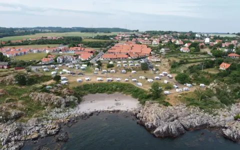 Sannes familjecamping vid kusten, med husvagnar och tält utspridda bland klippor och grönska.