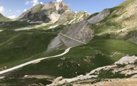 Strada bianca serpeggia tra verdi colline e rocce, verso un monte imponente. Un'avventura in **moto** su una **colle fauniera** panoramica.
