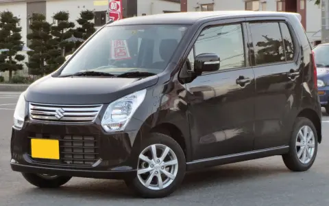Ciemny Suzuki Wagon R+ z żółtą tablicą rejestracyjną, zaparkowany na ulicy.