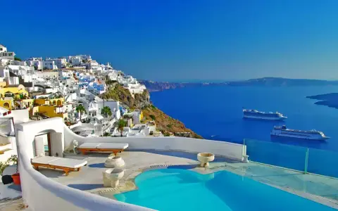 Vista mozzafiato di Santorini con case bianche a picco sul mare blu intenso. Due navi da crociera all'orizzonte, un invito a scoprire crociere a prezzi stracciati.