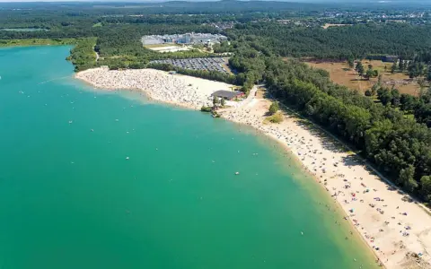 Sonniger Tag am **Silbersee Haltern am See**. Tausende Besucher genießen das türkisfarbene Wasser und den breiten Sandstrand, umgeben von grünen Wäldern.