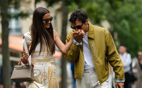 Ein Mann küsst die Hand einer Frau. Ihr **outfit erstes date** ist elegant: Sie trägt ein gemustertes Kleid, er eine olivgrüne Jacke.