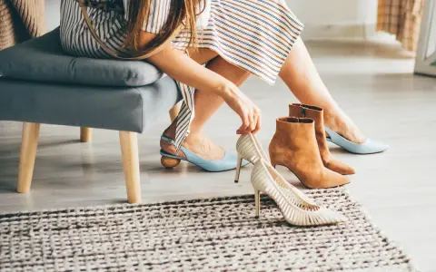 Kobieta przymierza buty, zastanawiając się, jak rozciągnąć buty, by były wygodniejsze. Na podłodze leżą jasne szpilki i brązowe botki.