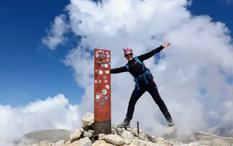Donna esulta in cima al Monte Amaro dopo un trekking. Cielo azzurro e nuvole bianche.