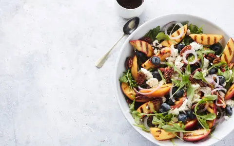 Salat mit Nektarinen, Blaubeeren, Ziegenkäse und Pekannüssen, garniert mit roten Zwiebelringen.