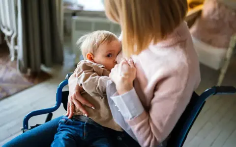Mama w wózku inwalidzkim karmi piersią dziecko. Wkrótce nadejdzie czas, jak odstawić dziecko od karmienia piersią, ale teraz liczy się bliskość.