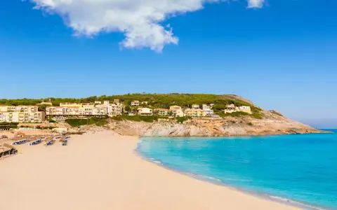 Traumhafter **Spanien Strand** mit feinem Sand, türkisfarbenem Meer und Hotels auf einem Hügel.