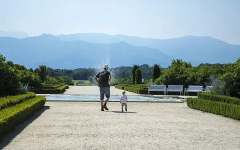 Un uomo e un bambino passeggiano in un giardino curato, con fontane e montagne sullo sfondo. Una giornata perfetta in Piemonte con bambini.