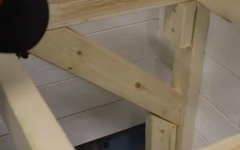 En person håller på att såga snett en träbit som ska bli en del av en konstruktion.