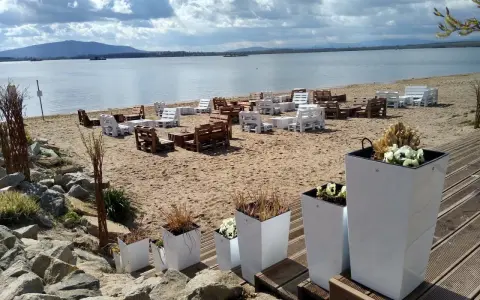 Plaża nad mietkowym zalewem z meblami z palet. W oddali góra i jezioro.