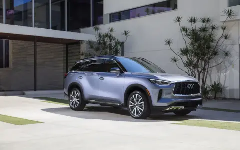 Elegancki, srebrny infiniti samochód zaparkowany przed nowoczesnym budynkiem z kamienną fasadą i dużymi oknami.