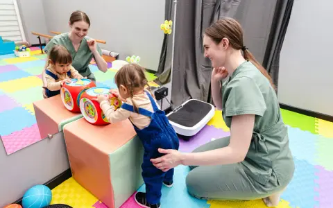 Dwie małe dziewczynki bawią się interaktywną kostką, a fizjoterapeutka wspiera jedną z nich. To może być część terapii wwr co to.