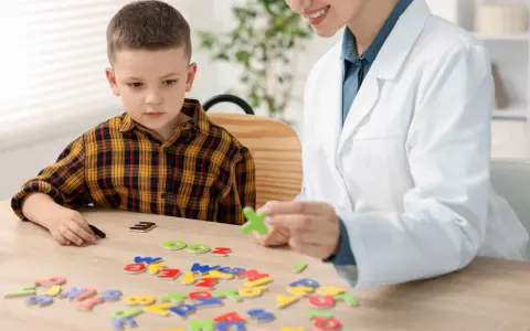 Chłopiec z dysleksją układa litery z terapeutką. Czy dysleksja to choroba? Terapia pomaga w nauce.