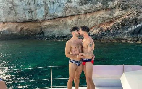 A loving gay couple shares a kiss on a boat, enjoying the stunning scenery of the Canary Islands.