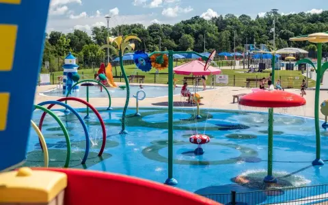 Kolorowy wodny plac zabaw z atrakcjami dla dzieci w Krosnie. Dzieci pluskają się w wodzie pod kolorowymi parasolami i zraszczaczami.