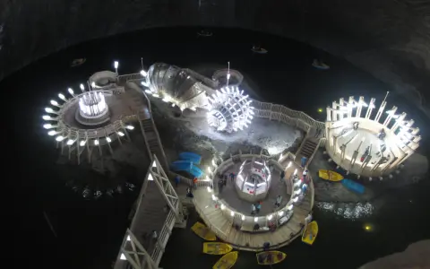 Podziemne jezioro w **Salina Turda** z łódkami i oświetlonymi platformami.