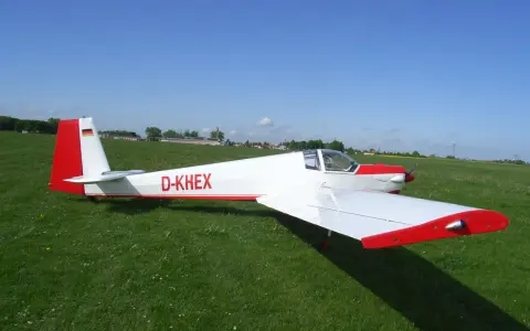 Ein weißer Motorsegler Falke mit roten Akzenten steht auf einer grünen Wiese.