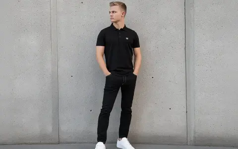 Młody mężczyzna w czarnej koszulce polo i jeansach pokazuje, jak nosić koszulkę polo na co dzień.