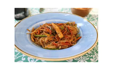 Un piatto di spaghetti di riso con verdure colorate, tra cui peperoni, carote e pannocchiette, condito con una salsa saporita.
