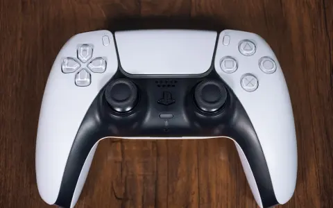 Biały kontroler DualSense do PS5 leży na drewnianym blacie. Zastanawiasz się nad ps4 pobór prądu?