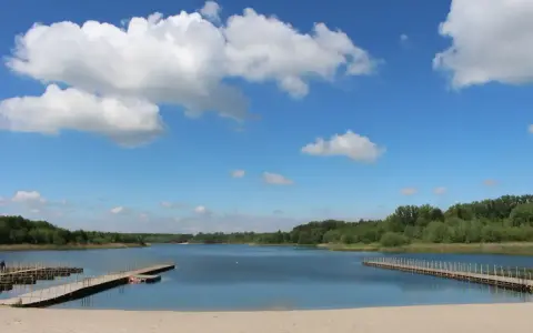Piękny dzień nad jeziorem Wilczyńskim. Piaszczysta plaża, drewniane pomosty i błękitne niebo z białymi chmurami zapraszają do wypoczynku.
