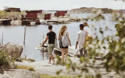Vänner njuter av en promenad längs vattnet vid röda fiskestugor, en perfekt bild av eco tourism i Sverige.