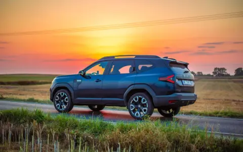 Ciemnoniebieski Dacia Bigster 2025 na tle zachodzącego słońca, na wiejskiej drodze.