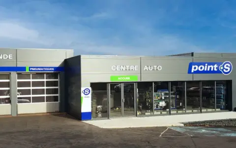 Façade d'un centre auto Point S avec des portes de garage et des panneaux indiquant les services (vidange, freins, pneumatiques, pare-brise).