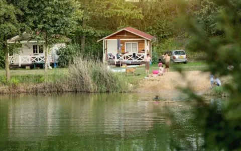 Rodzina odpoczywa nad jeziorem w malowniczym miejscu. Dzieci pluskają się w wodzie, a dorośli relaksują się na plaży przy domkach kempingowych. To idealne miejsce na rodzinne wakacje, prawdziwa **camping forteca** spokoju i radości.