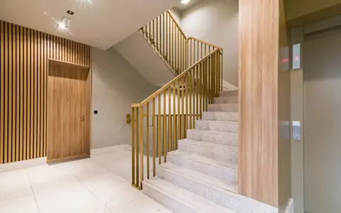 Nowoczesna klatka schodowa z drewnianą okładziną i złotymi balustradami. Osłona ściany przy schodach podkreśla elegancję wnętrza.