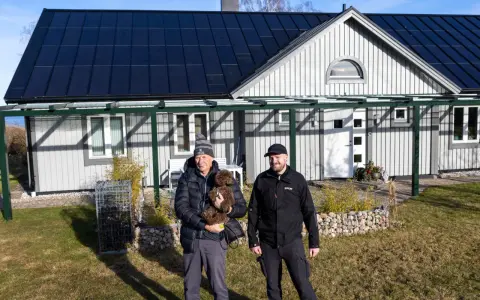 Två män och en hund framför ett hus med solpaneler på taket. Taket har vackra vinklar som ger huset karaktär.