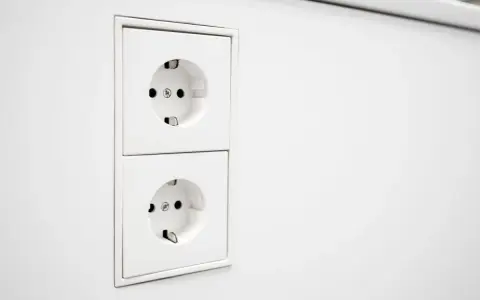 Deux prises EU blanches, alignées verticalement sur un mur blanc. Prêtes à alimenter vos appareils.