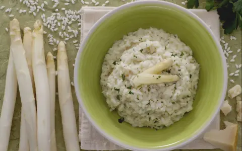 Delicioso risotto de espárragos cremoso, adornado con espárragos blancos y perejil picado. Acompañado de espárragos frescos y trozos de queso parmesano.