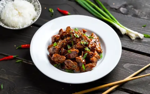 Pyszny kurczak luc lac w sosie, posypany szczypiorkiem i sezamem, obok miseczka ryżu, pałeczki i papryczki chili.