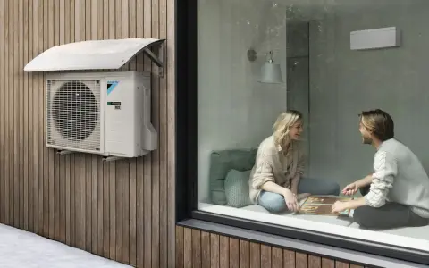 Unidad exterior de aire acondicionado Daikin instalada bajo un alero protector en una pared de madera. Ideal para saber donde colocar la unidad exterior del aire acondicionado.