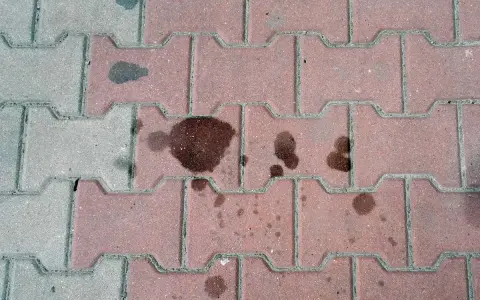 Stare plamy z oleju na kostce brukowej tworzą ciemne ślady, świadczące o dawnych wyciekach.